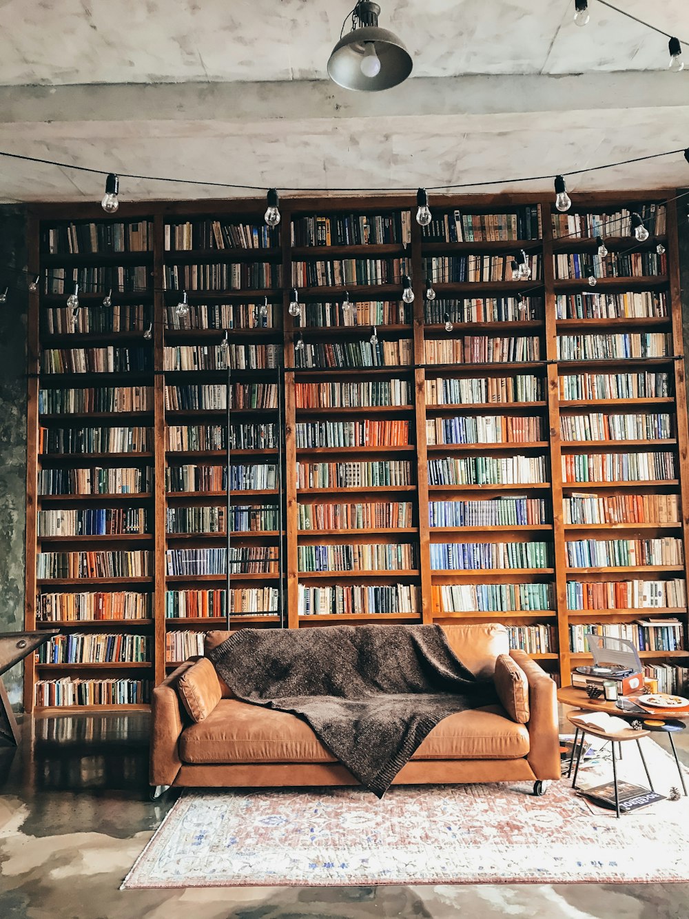 Boekenwand van vloer tot plafond, volgepakt met boeken, met een bank ervoor