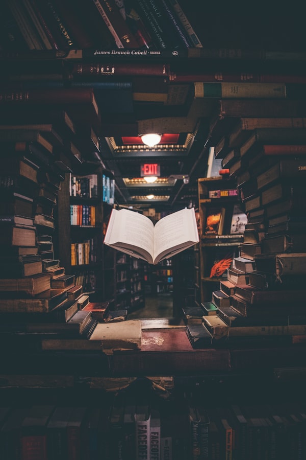 Doorkijkje tussen hoog opgestapelde boeken in een boekhandel, met in het midden een opengeslagen boek